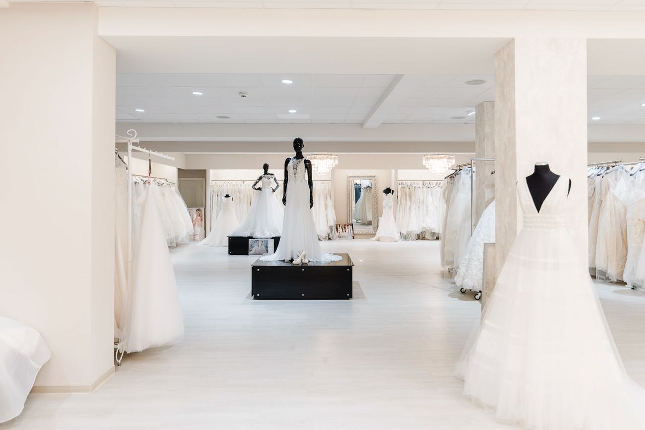 Ein modernes Brautmodengeschäft mit eleganten Brautkleid-Designs auf Schaufensterpuppen und Regalen sowie Festmode für besondere Anlässe, die in einem großzügigen, hellen Raum präsentiert werden.